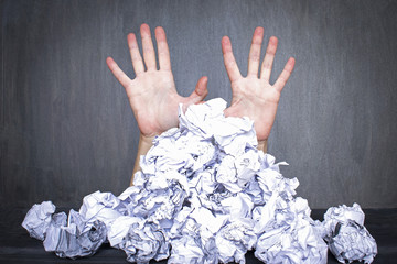 Too much work or lack of inspiration concept, pile of crumpled paper and woman`s hands behind it, black background.