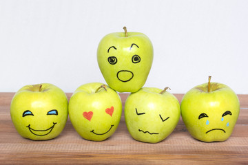 Different emotions drawn on apples, wooden background.