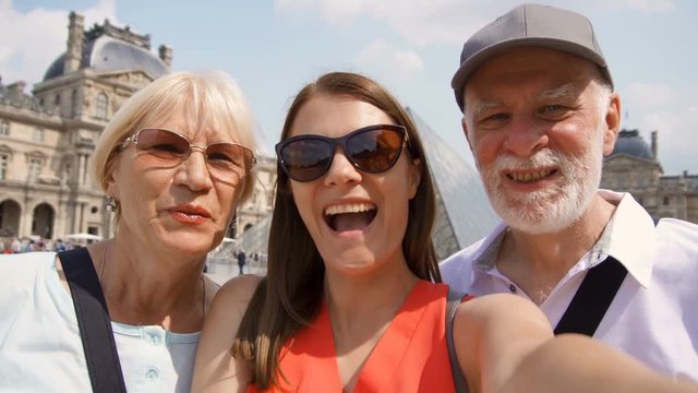 Happy family of senior man and woman with daughter taking selfie on smartphone on vacation in Paris. Daughter kissing her mother. Place du Carrousel