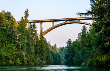 Scenic highway bridge extending over flowing river waters. Beautiful nature landscape scene of forest with river water with vantage point view of bridge from underneath.