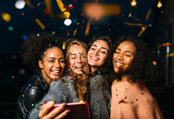 Group of happy women taking selfie on mobile phone, standing outdoors at night