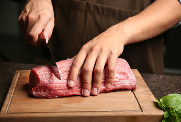 Chef cutting fresh raw meat on wooden board