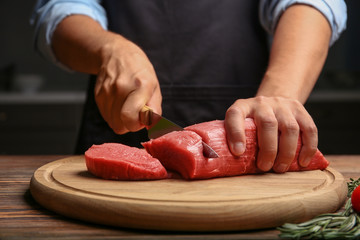 Chef cutting fresh raw meat on wooden board