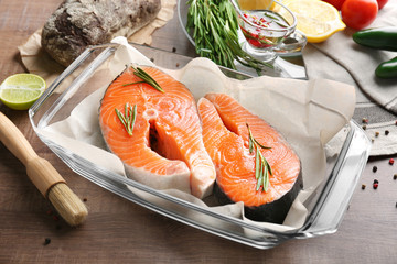 Fresh salmon steaks in baking dish on wooden table