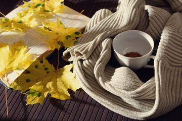 The c Cup of instant coffee, a book, a sweater and autumn leaves illuminated by sunlight from the window. Toned