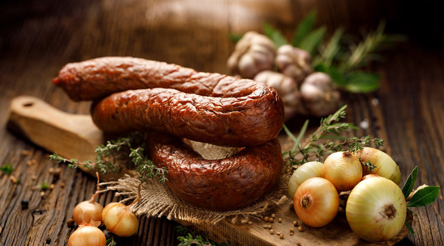 Smoked  sausage on a wooden rustic table with addition of fresh aromatic herbs and spices, natural product from organic farm, produced by traditional methods