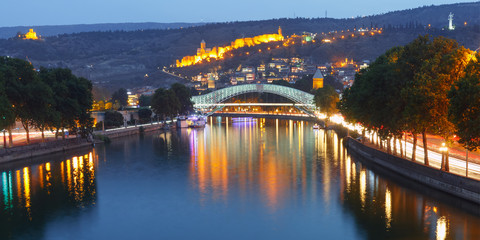 Panorama of night Old Town with Narikala Fortress and illuminated Bridge of Peace across Kura river, Tbilisi, Georgia - obrazy, fototapety, plakaty