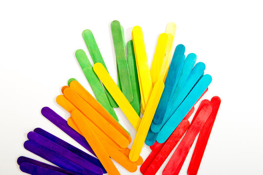 Rainbow colored wooden sticks scattered against white background