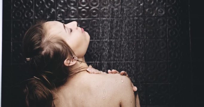 Woman taking shower in slow motion 120fps.Young beautiful woman taking a shower and gently touching her skin, smiling turning to the camera. Beauty and wellbeing concept. Filmed in 4K DCi RAW. 