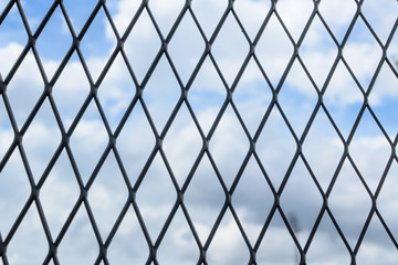 Black solid metallic mesh fence closeup with sky in the background.