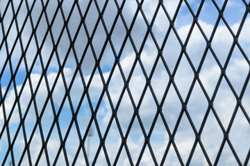 Black solid metallic mesh fence closeup with sky in the background.