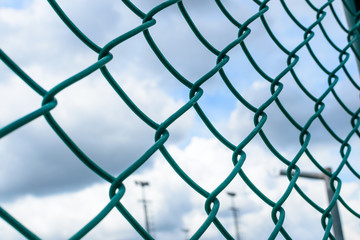 Fototapeta premium Green metal wire fence under fluffy white clouds and blue sky background.