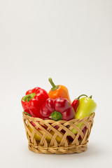 Several ripe sweet and hot peppers in a straw basket on a white background