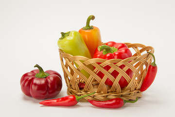 Fototapeta na wymiar Several ripe sweet and hot peppers in a straw basket on a white background