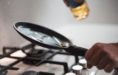 A man cook in a nice apron prepares an omelette in a frying pan on a glass gas hob