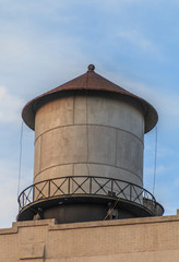 Metal water tank sitting on top of a building. The water tank has a peaked reddish brown roof. It has a metal walkway around it.