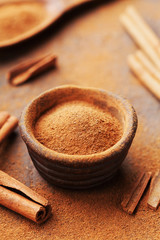 Pile of cinnamon sticks and powder on brown rustic background. Aromatic spices.