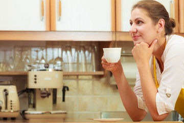 Mature woman drinking cup of coffee in kitchen.