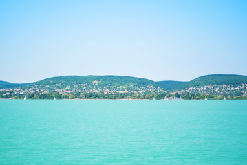Fototapeta premium A view from a ship to bright Balaton lake water and coast at the background on sunny summer day, Hungary.