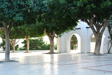 A view of bright white building with arch and green trees in the street of small mediterranean town Torremolinos, Andalusia, Spain.