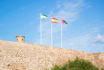 Bright colorful flags over the ancient stone wall of Gibralfaro castle (Alcazaba de Malaga) over the mountain with a bright blue sky at the background on sunny day.