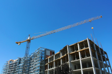 Unfinished building of apartment house under construction and a crane on sunny day with blue sky at the background.