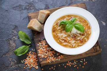 Glass plate of italian soup with lentils and pasta on a rustic wooden serving board, studio shot