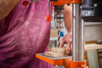 Close-up of a man with work clothes, a carpenter drilling a wooden board on an orange large...