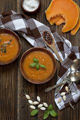 Traditional pumpkin homemade cream-soup with seeds and basil on the rustic wooden background. Close up, selective focus