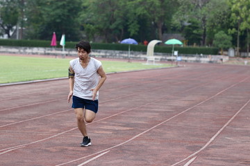 Handsome athlete Asian man running on racetrack in stadium with copy space background. Healthy active lifestyle concept.