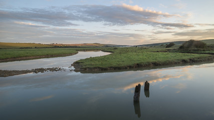 Beautiful dawn landscape over English countryside with river slowly flowing through fields