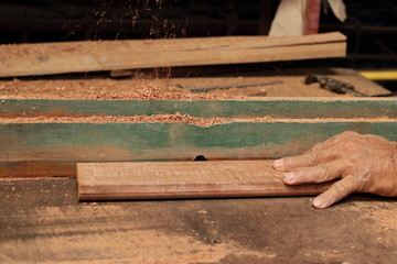 Hands of senior carpenter shaving a piece of wood on router table in carpentry workshop.