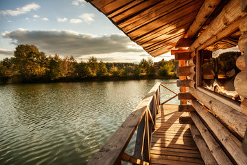 Wooden house with a terrace on the water at the lake, at sunset, a beautiful river bank at sunset