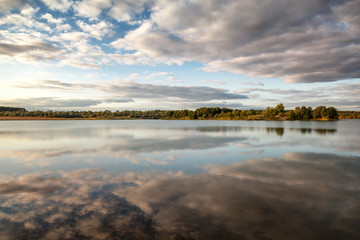 Fototapeta premium A beautiful autumn landscape, a forest reflected in a river, the sky with clouds.