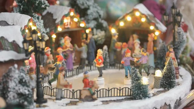 Close-up - miniature souvenir Christmas toy - little people skate in circle on an ice rink illuminated with garland with winter scenery