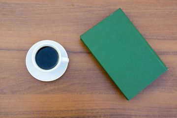 Cup of coffee and closed book on wooden table