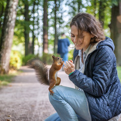 Beautiful young woman feeding a squirrel in an autumn park, a squirrel sitting on a girl © olezzo