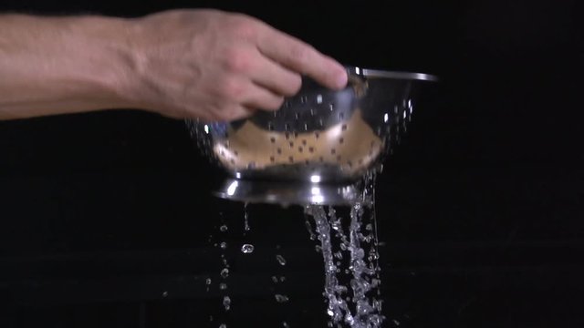 Man&rsquo;s hands raise the colander from which slowly drops of water drip. Super slow motion.
