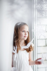 A girl  sits by the window among the paper snowflakes