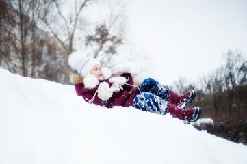 A girl in winter clothes rides on her back with a snow slide