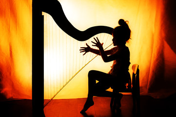 Silhouettes of the girl sitting on a chair and playing the harp