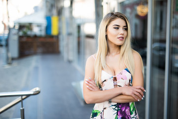 Young beautiful blonde woman in light dress posing outside with wall in background.