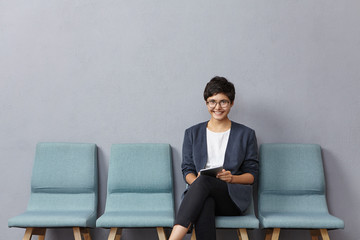 Indoor shot of positive business lady comes in polyclinic, makes appointemnt to doctor, sits in...