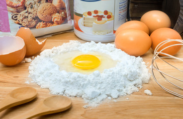 flour with egg and ingredients for homemade bakery on wooden background