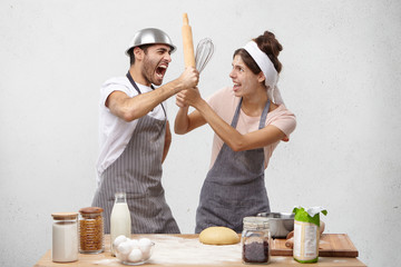 Furious outraged man finds out about wife`s betrayal, fight with kitchen untensils, screams in bewilderment and panic. Cook competitiors have battle at work place, defend by rolling pin and whisk