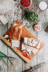 homemade bacon cut into thin pieces with the salt and spices on a wooden Board