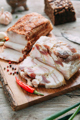 homemade bacon cut into thin pieces with the salt and spices on a wooden Board
