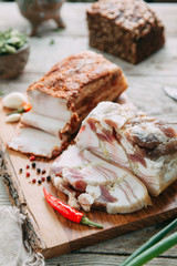 homemade bacon cut into thin pieces with the salt and spices on a wooden Board