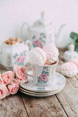 tea set in composition with flowers and marshmallows. Coffee mug on a saucer, a teapot and a sugar bowl. Filmed in the interior