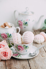tea set in composition with flowers and marshmallows. Coffee mug on a saucer, a teapot and a sugar bowl. Filmed in the interior